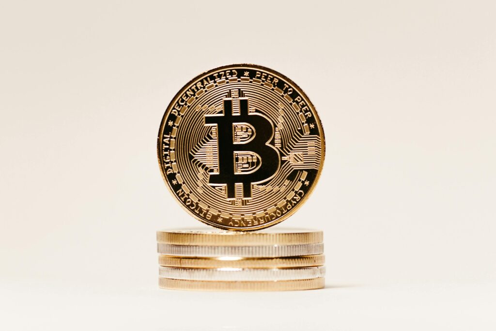 pexels-photo-14902667-14902667 Close-up of a golden Bitcoin symbol coin on stacked coins with a white background, perfect for finance and technology content.