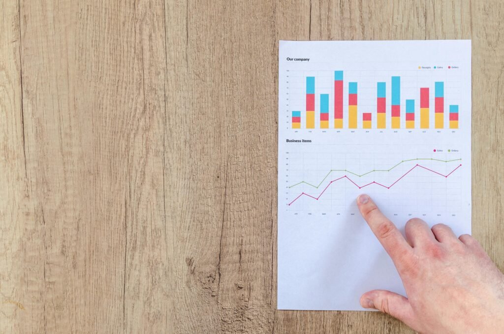 Business Partner 1 Hand analyzing business graphs on a wooden desk, focusing on data results and growth analysis.