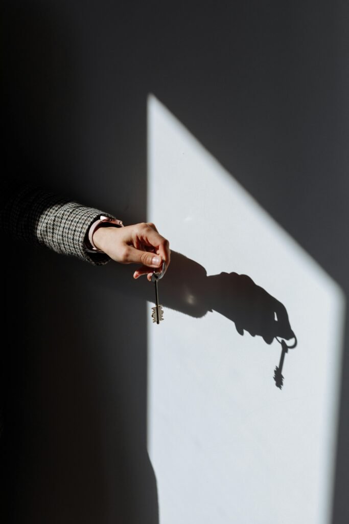 pexels-photo-8470841-8470841 Hand with a key casting a dramatic shadow on a wall, symbolizing property or ownership.